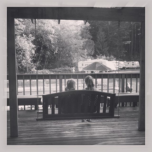 a picture of two young girls from behind sitting on a porch swing