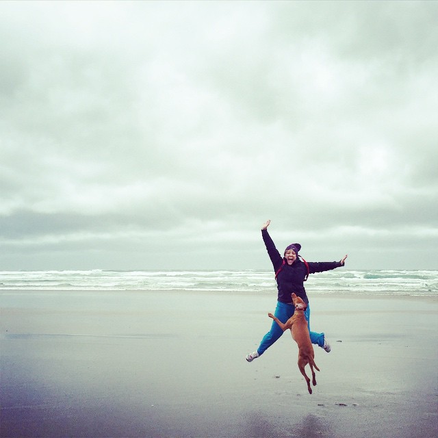 woman and dog jumping on a beach in the rain and wind